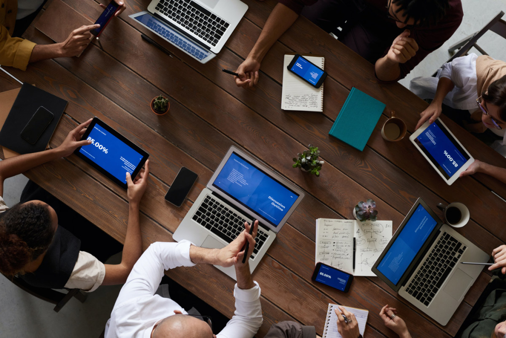 A group of people are sitting at a table; they each have their own laptop or tablet, but it's clear that they work together.