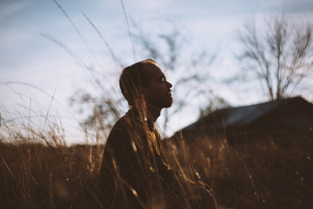 A person sits in a lotus position in the grass and meditates; the setting sun illuminates his face.