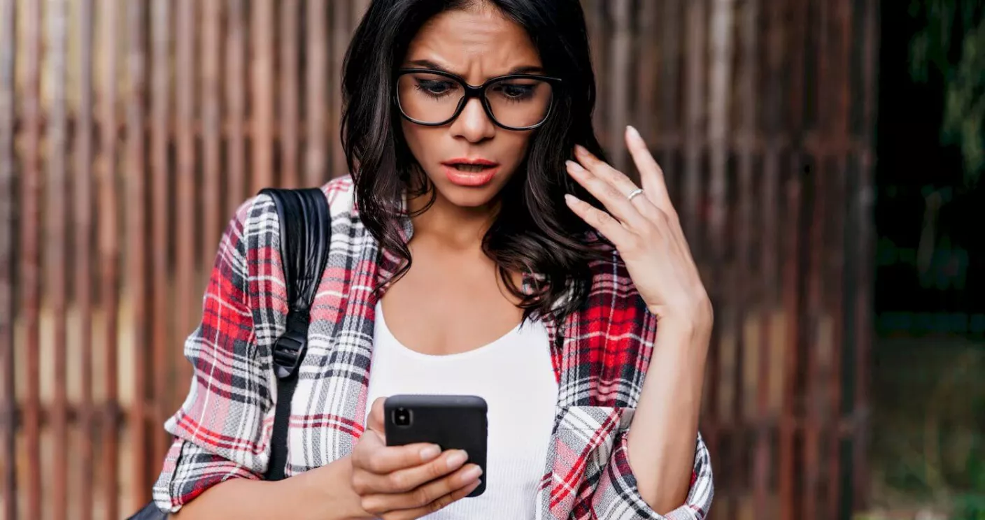 A young college student looking shocked at her phone.