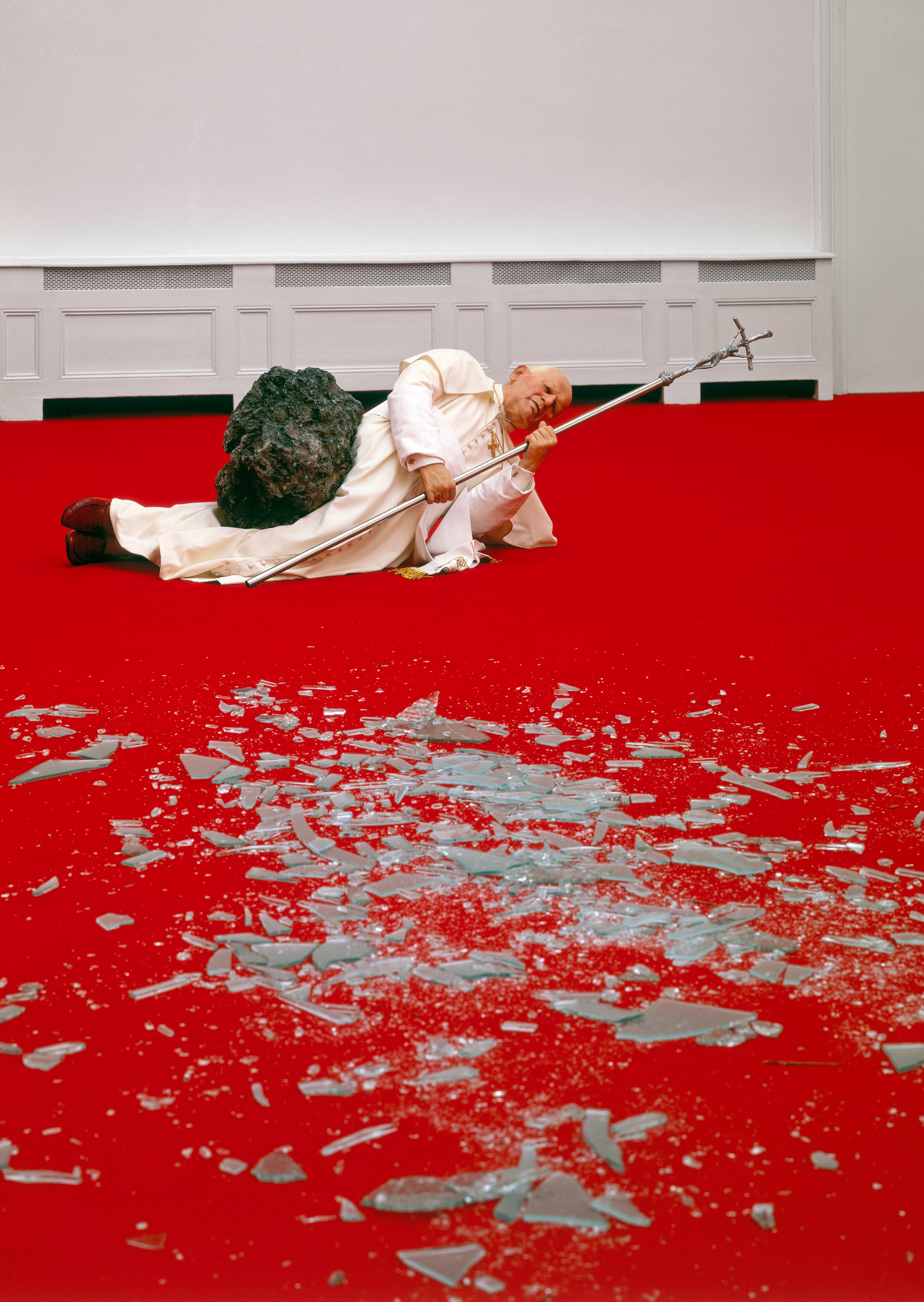 Pope John Paul II clad in his full ceremonial attire, lying beneath a meteorite that has crashed through a glass ceiling and is about to crush him