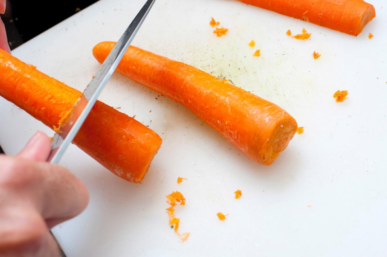 Preparing the carrots by scraping them with an ordinary knife.
