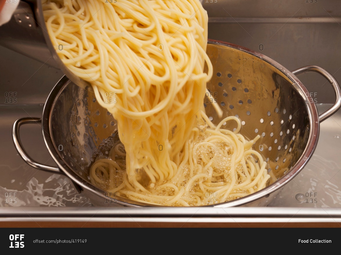 Putting the pasta into the colander inside the sink.